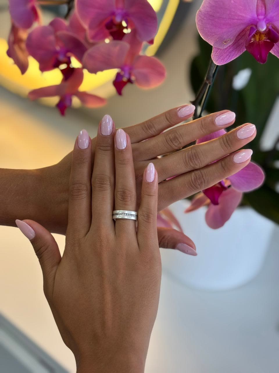 Unhas feitas no salão, com orquídeas ao fundo